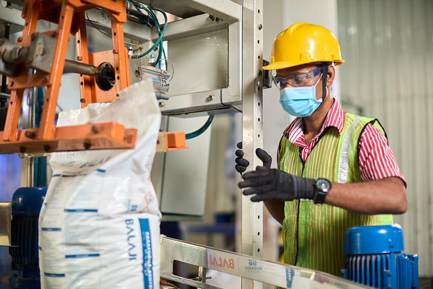 Worker in gloves and mask standing near machine swaling the white bag at Formaldehyde Production unit